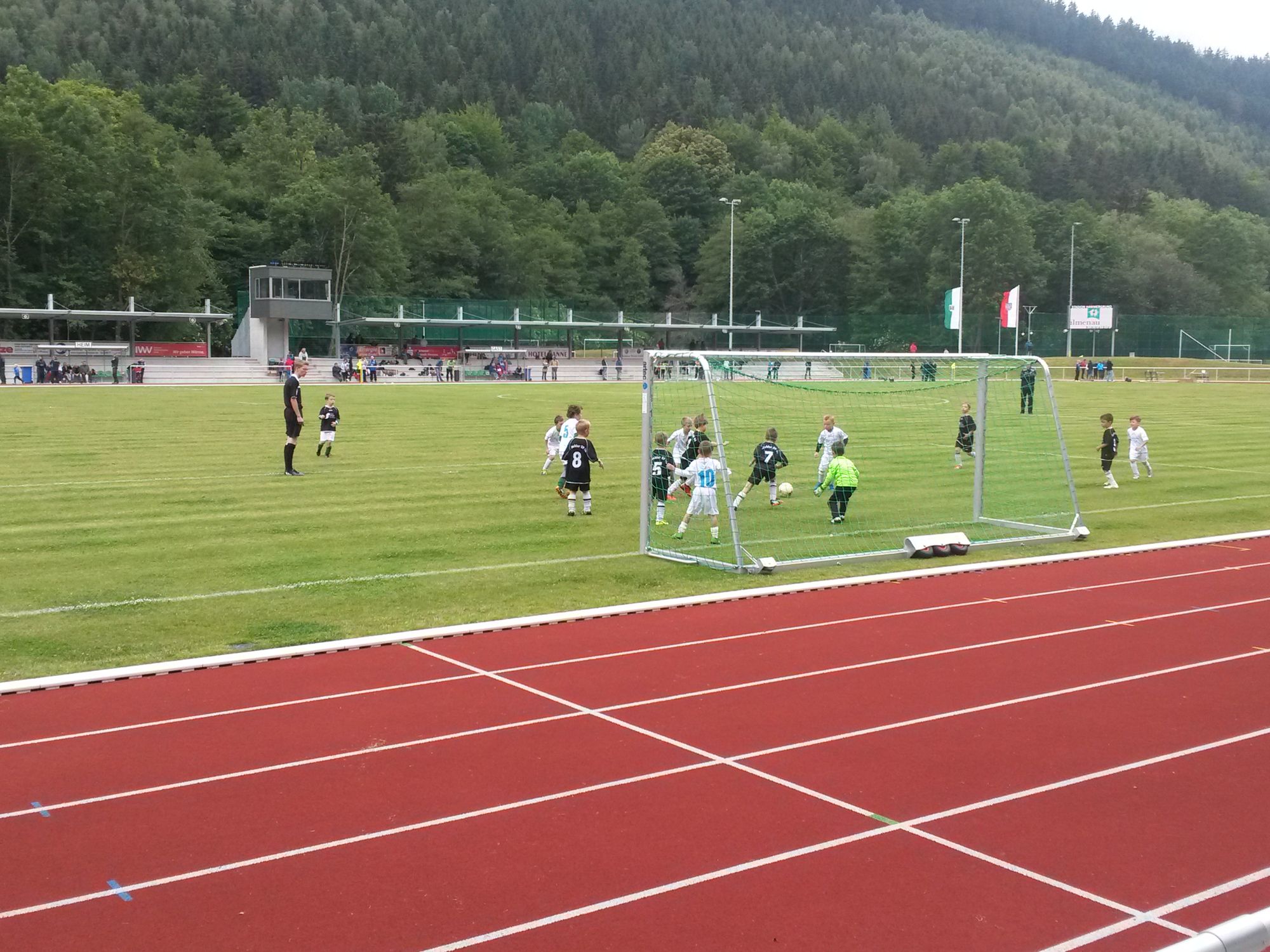 Sportanlage mit roter Kunststofflaufbahn und Rasenspielfeld, auf dem Kinder trainieren